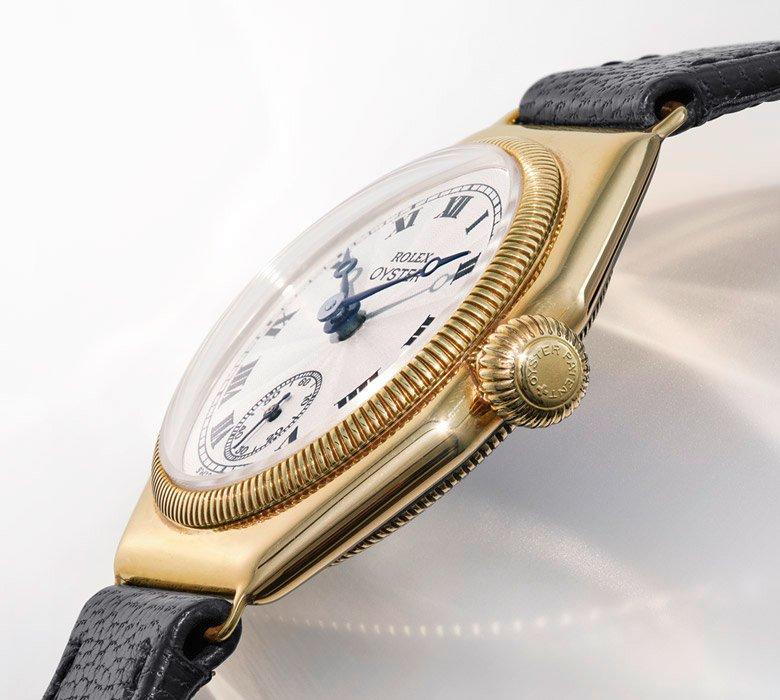 Close-up of a gold Rolex Oyster watch with a white dial, Roman numerals, black hands, and a black leather strap.